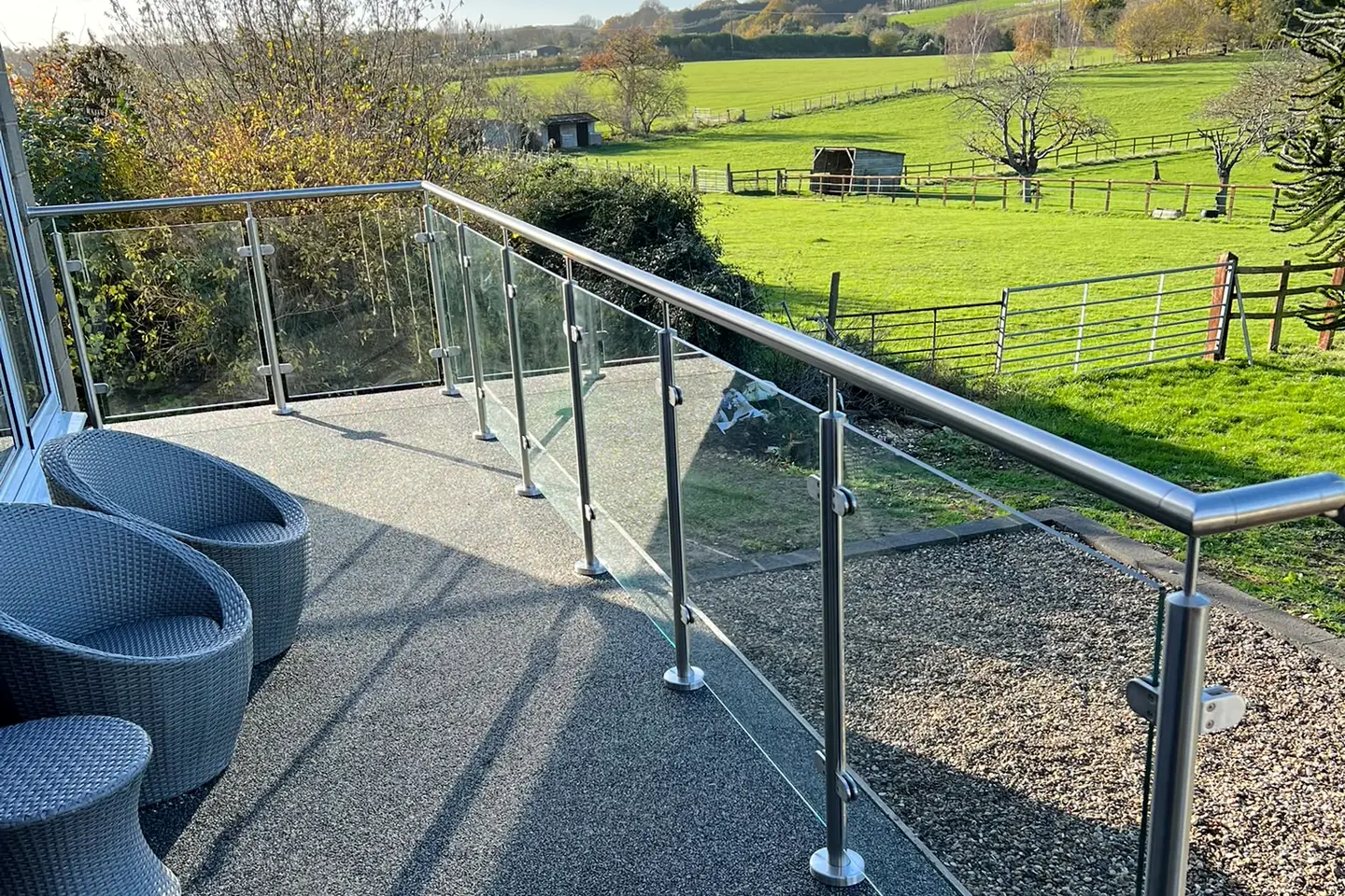 A stainless steel and glass rail around a deck, looking out over fields